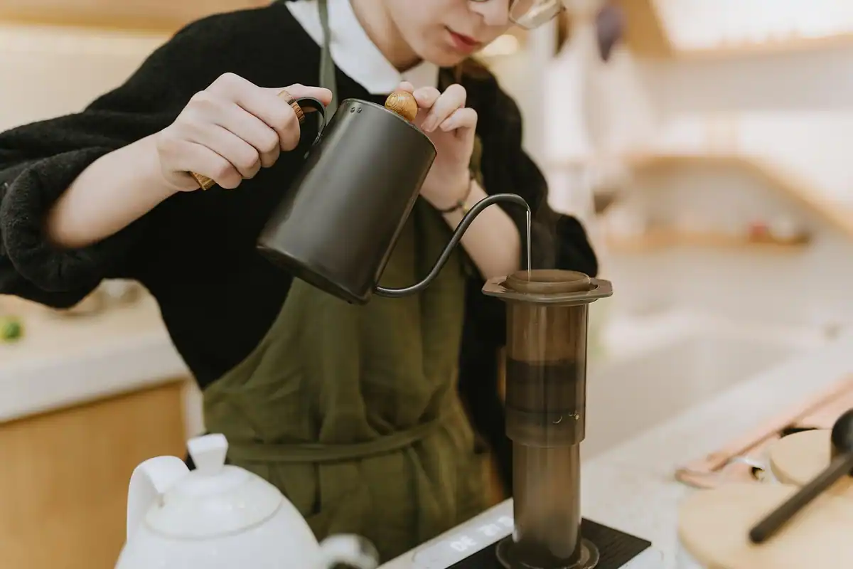 Tânăr în șorț care toarnă apă fierbinte într-un filtru de cafea, la prima slujbă de vară