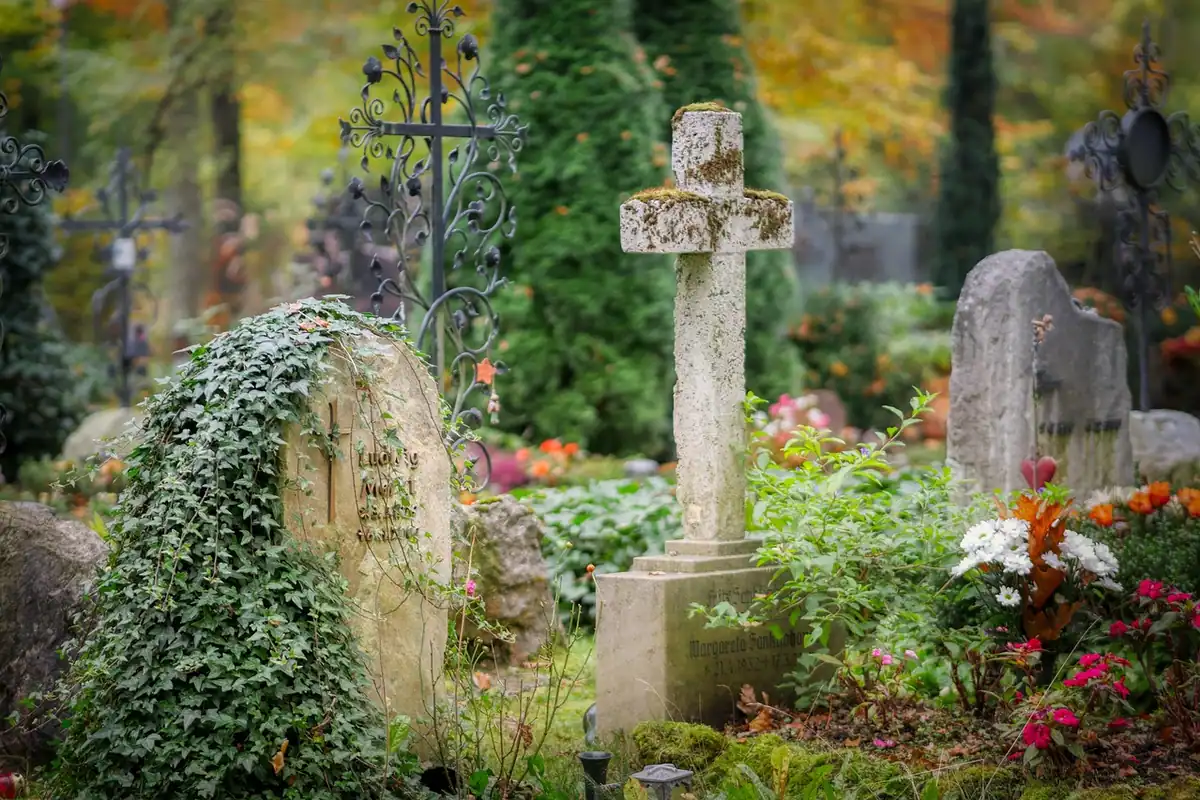 Cruce de piatră și morminte printre flori, într-un cimitir îngrijit