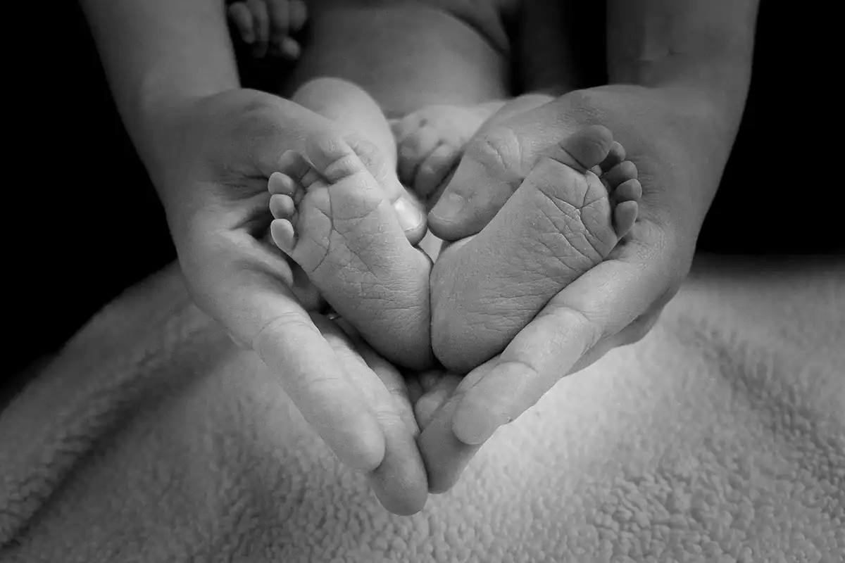 Mâini care țin ocrotitor tălpile unui nou-născut, pentru alocația de stat a copilului