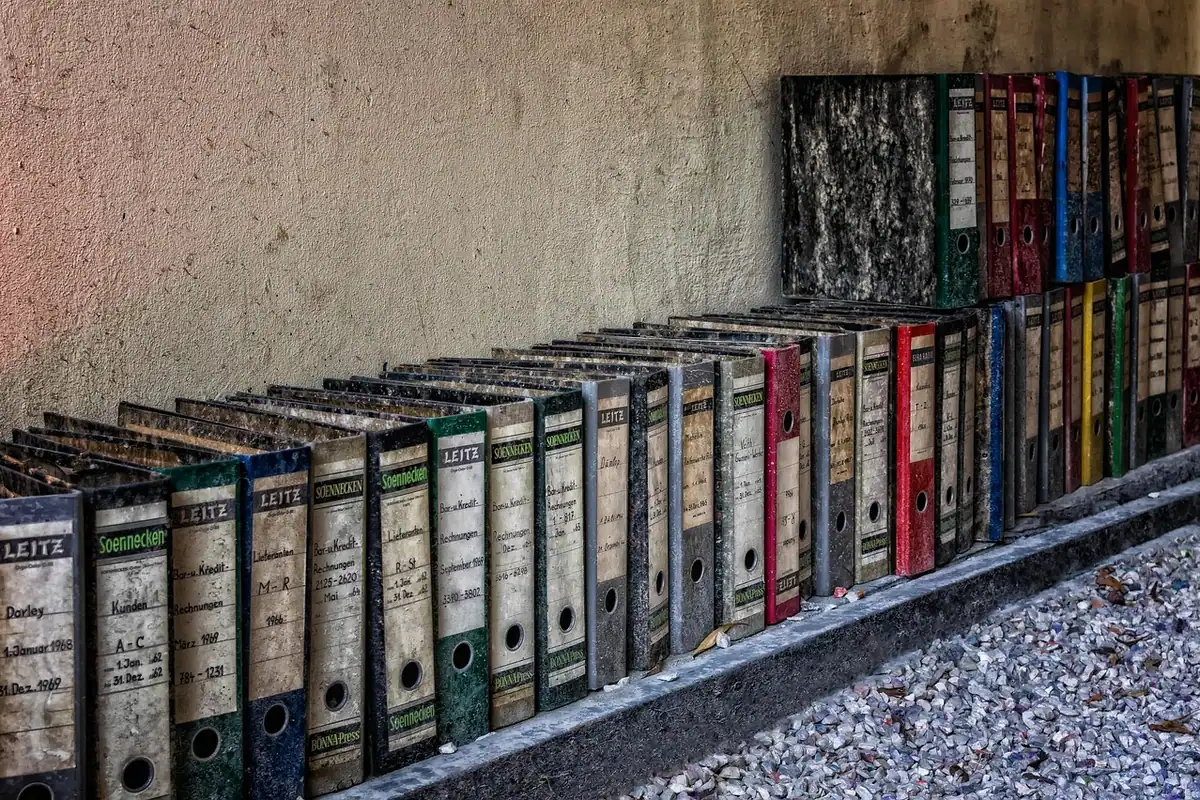 Rând lung de bibliorafturi colorate pe un raft, unde se păstrează dosarele cu actele de muncă