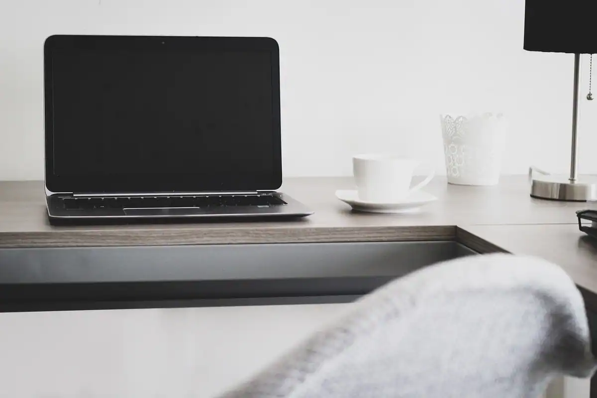 Laptop deschis pe un birou alb lângă o ceașcă, pentru plata online a contribuției voluntare