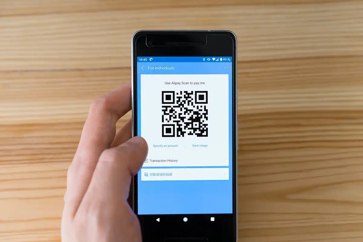 Mână care ține un telefon cu cod QR pe ecran, pentru plățile digitale