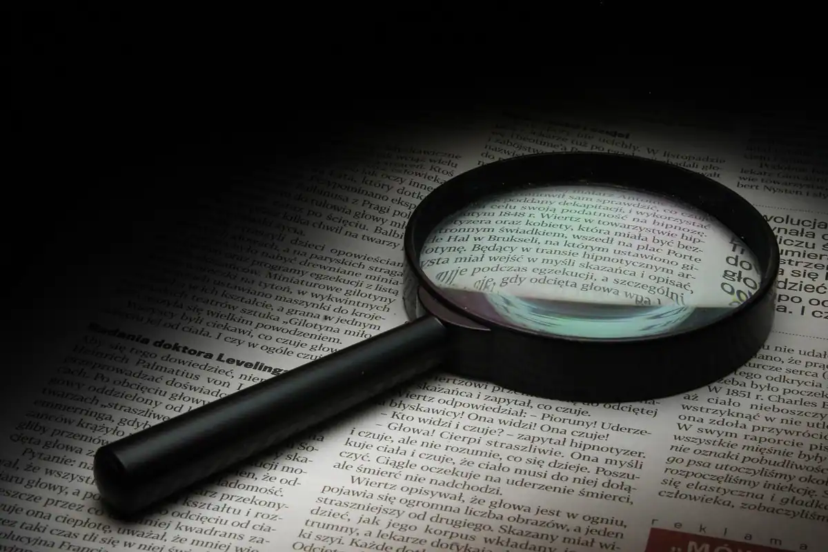 Lupă mare așezată pe un text tipărit, pentru citirea atentă a comisioanelor