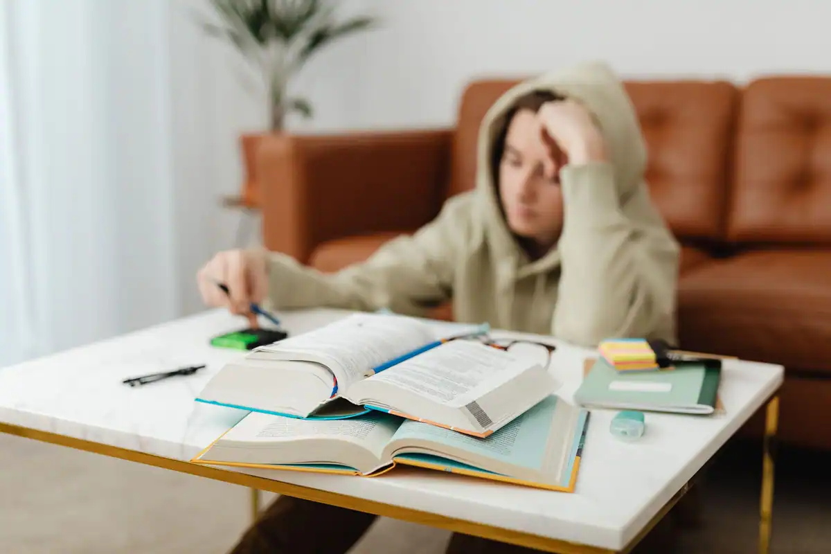 Student concentrat la o masă albă plină de cărți și notițe