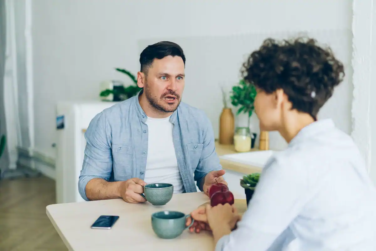 Un cuplu poartă o discuție serioasă la masa din bucătărie, cu cești de cafea în față