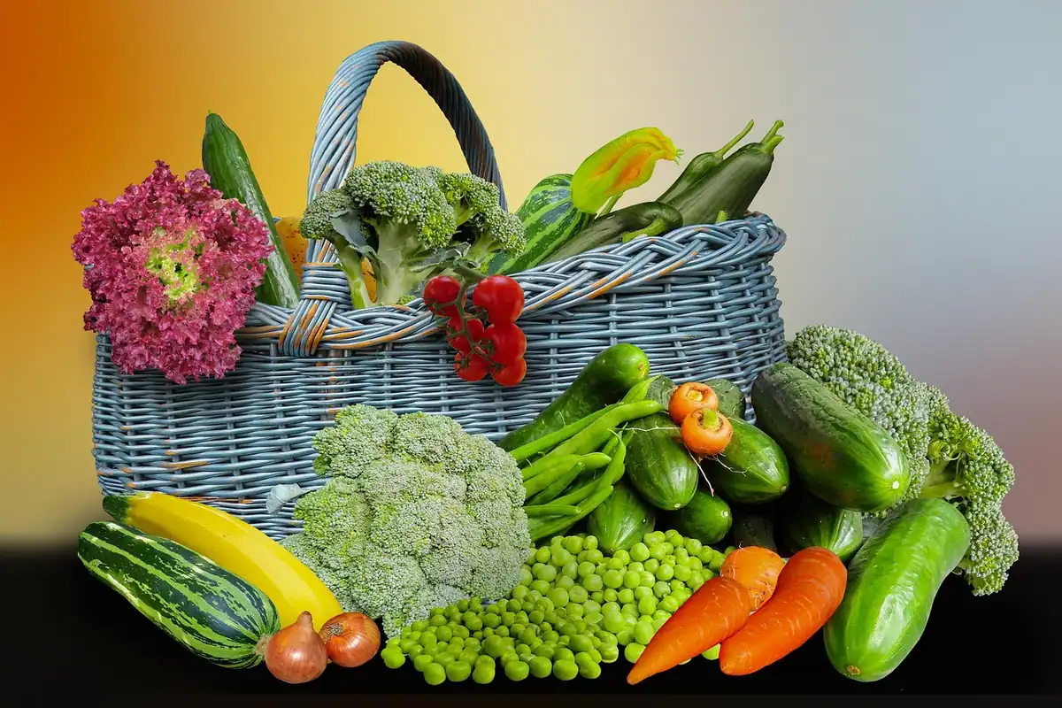 Coș împletit plin cu legume proaspete, broccoli, mazăre, morcovi și castraveți, pentru nevoi de bază
