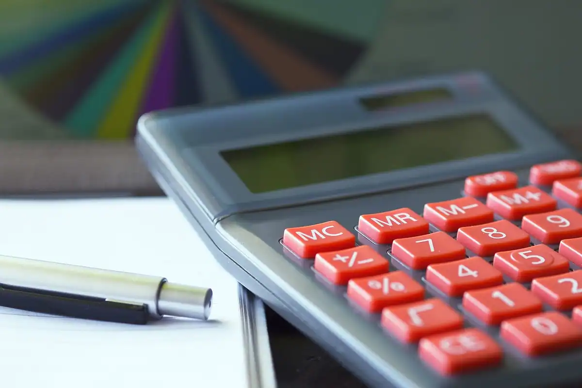 Calculator cu taste roșii lângă un stilou, pe un birou de contabilitate