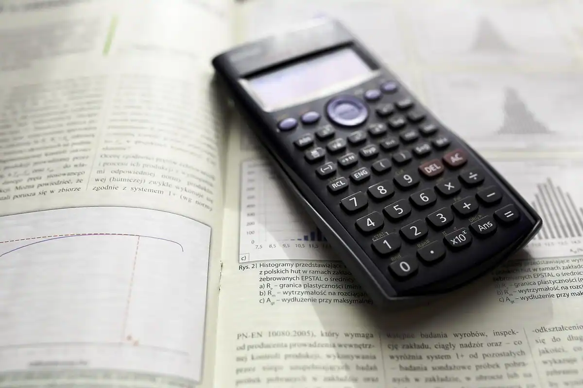 Calculator științific negru așezat pe o carte deschisă cu tabele și grafice