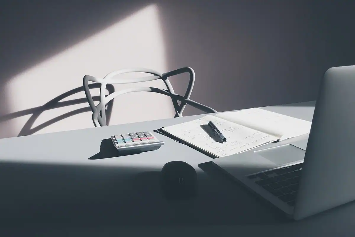 Birou cu laptop, caiet, stilou și calculator mic, în lumina unei ferestre