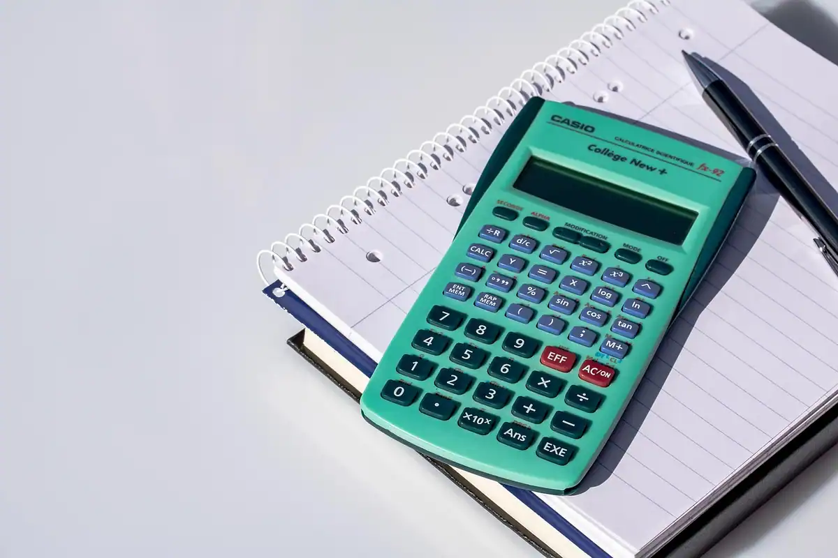 Calculator verde pe un caiet cu spirală, lângă un pix, pentru calculul ratei de înlocuire